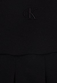 Černý ribbedový textilní oděv s vyšitým logem cK. Design zahrnuje plynulý přechod mezi horní a dolní částí.