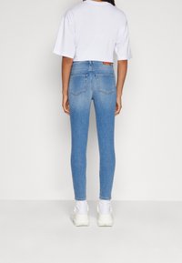 Jeans ajustados de color azul claro con una cintura alta, bolsillos traseros cosidos y un ligero desgaste. Combinados con una camiseta corta blanca y zapatillas blancas.