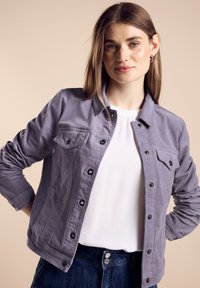 Lila bomulljacka med knäppning framtill, två bröstfickor och svarta knappar. Kombinerad med en vit topp och mörk denim.