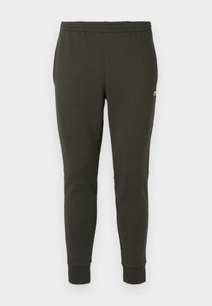 Sötétzöld, puha anyagból készült jogger nadrág, rugalmas derékkal, bordázott passzés szárakkal és egy kis logóval az oldalon.