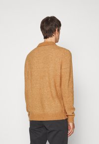 Kamelfärgad stickad tröja med mjukt material, ribbade ärmslut och nederkant, samt en klassisk kragsdesign som syns från baksidan.