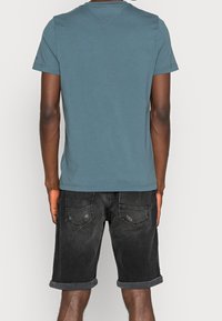 Modré bavlněné tričko s krátkými rukávy a kulatým výstřihem, ve spojení s černými denimovými šortkami, s ohrnutými nohavicemi, ukazující detaily zadního pohledu.