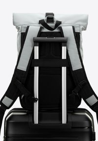 Valise noire robuste avec un sac à dos à rouleau gris attaché. Le sac à dos présente un rembourrage en maille noir et des sangles réglables. La poignée en aluminium est visible.