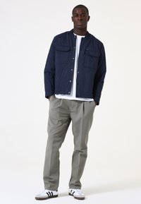Marineblaue gesteppte Bomberjacke mit zwei Brusttaschen, kombiniert mit hellgrauen Hosen und weißen Sneakers mit schwarzen Streifen.