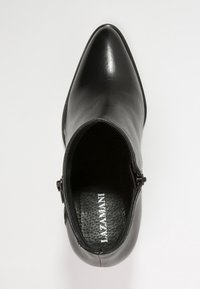 Zwarte leren enkelboot met spitse neus, zijklitser en getextureerde binnenzool gemarkeerd met "LIAZAMANI," van bovenaf weergegeven op een witte achtergrond.