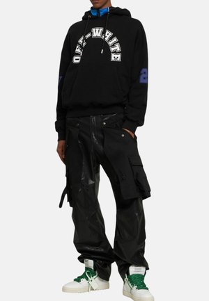 Schwarzer Hoodie mit weißem "OFF-WHITE"-Logo und blauen Akzenten, kombiniert mit schwarzen Cargo-Hosen mit Taschen und glänzenden Details. Weiße Sneaker mit grünen Schnürsenkeln.