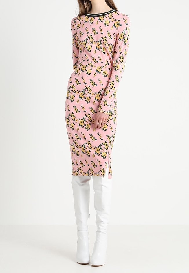 Robe à manches longues à fleurs roses avec des fleurs jaunes, une fente latérale et un col noir, assortie à des bottes blanches montant jusqu'aux genoux.