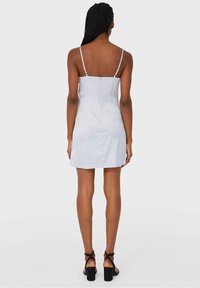 Robe spaghetti de couleur gris clair avec un dos ajusté, fermeture éclair et un ourlet droit. Portée avec des sandales à talons blocs noires.