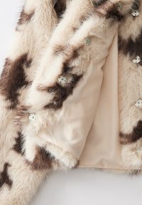 Faux fur jas met een crèmekleurig en bruinen patroon, voorzien van een satijnen binnenvoering en ronde, doorzichtige knopen aan de voorkant voor sluiting.