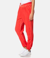 Rdeče bombažne jogger hlače z elastičnim pasom, stranskimi žepi in belim vrvico. Imajo belo stransko obrobo. Nosijo se z belimi športnimi copati.