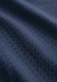 Țesătură texturată de culoare bleu marin, cu un model geometric, având o suprafață moale la atingere și detalii țesute intricate.