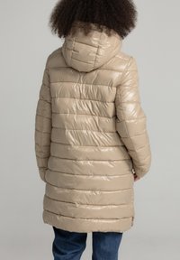 Beige gewatteerde jas met een capuchon, met een glanzende afwerking en horizontaal gestikte ontwerp. De jas reikt tot halverwege de dijen en heeft zijzakken.