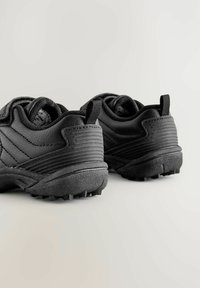 Zwarte sportieve schoenen met een gestructureerde synthetische bovenkant, rubberen zool en een trekband aan de achterkant. Kenmerkt een robuusteloop voor grip en gelaagde ontwerpaccenten.