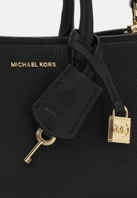 Sac à main en cuir noir avec des finitions en or. Présente un accent clé et une étiquette affichant le nom de la marque "Michael Kors". Surface texturée.