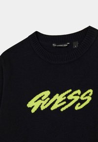 Maglione nero a maglia con la scritta "GUESS" in grassetto verde neon. Collo e polsini a coste, finitura testurizzata. Etichetta della taglia visibile all'interno.