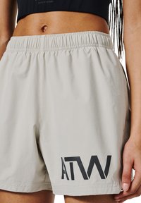 Ljusbeiga träningsshorts med resårmidja, med en framträdande svart "ATW"-logotyp på nedre vänstra sidan och en slät yta.