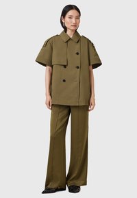 Olive zielona, oversize'owa kurtka koszulowa z podwójnym zapięciem i krótkimi rękawami, w zestawie z dopasowanymi spodniami o szerokich nogawkach. Gładki materiał, czarne guziki.