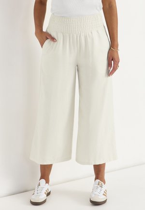 Person iført løse, højtaljede, vide, korte hvide bukser med lommer, parret med hvide sneakers og en hvid top.