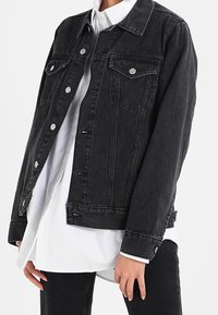 Czarna kurtka jeansowa o klasycznym kroju, z zapięciem na guziki, dwoma kieszeniami na piersi i lekko postrzępionym dołem.