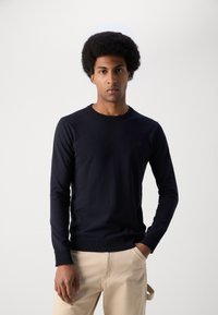Navy blue long-sleeve sweater with a round neckline and ribbed cuffs, made of a soft fabric, paired with light beige trousers.