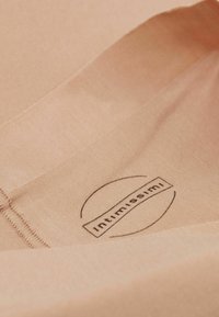 Licht perzikkleurige stof met een gladde textuur, voorzien van genaaide randen en een gedrukt logo met de tekst "intimissimi" binnen een cirkelontwerp.