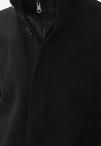 Svart ullkappa med huva, med dragkedjestängning och två knappar, slät textur och rena linjer. Inga synliga mönster eller detaljer.