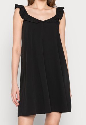 Czarna sukienka bez rękawów z falbanami przy kwadratowym dekolcie, noszona przez osobę o jasnej karnacji i brązowych włosach.