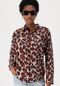 Leopard print button-up shirt in soft, lightweight fabric. Features a classic collar and long sleeves. Accents in black and rust tones.