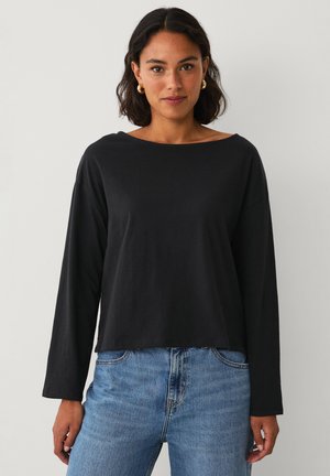 Zwarte lange mouwen top met een brede halslijn, relaxte pasvorm en zachte katoenen stof. Gekleed met lichtblauwe jeans met een vervaagde textuur.