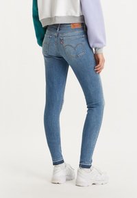 Smala blå jeans i denim med medelblå tvätt, två bakfickor och lätt slitage vid fållen, som är parat med vita sneakers.