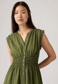 Zaļš kleitas apģērbs ar īsām piedurknēm, ar smalku vidukļa detalizāciju un plūstošu svārku. Izgatavota no viegla auduma ar mīkstu tekstūru.