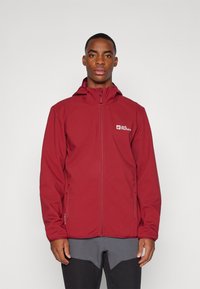 Rød softshell-jakke med lynlåslukning, justerbar hætte, logo på venstre bryst og lynlåslommer i siden. Fremstillet af et glat, let materiale.