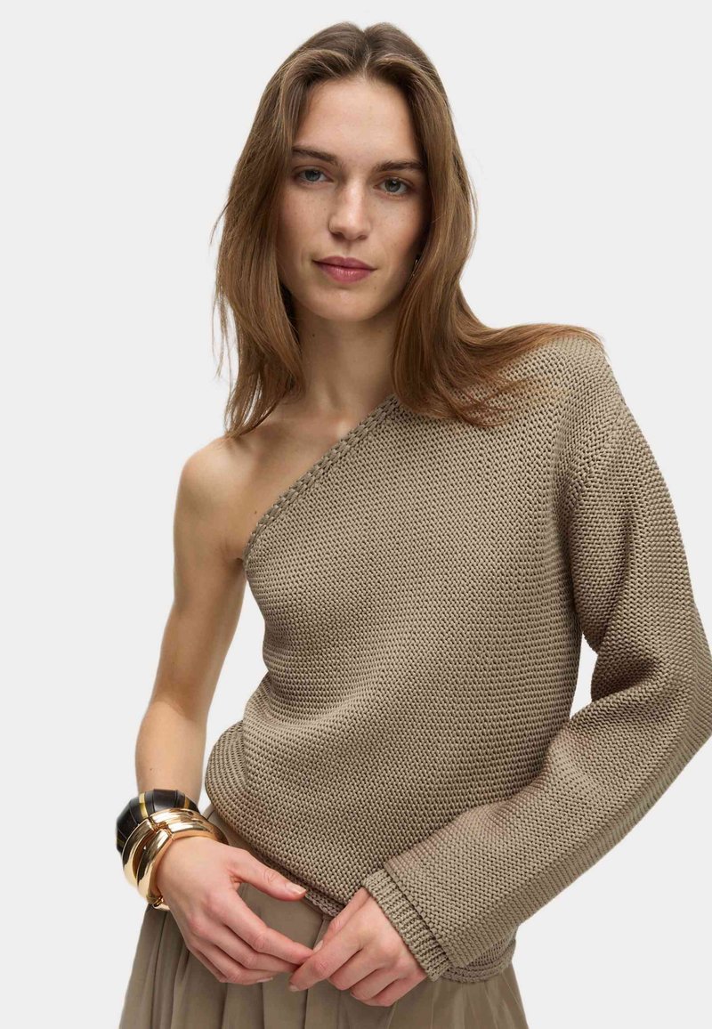 Pull en tricot beige avec une épaule dénudée. Tissu texturé, manche longue d'un côté, fini avec de délicates coutures.
