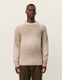 Beige neulepaita, jossa on liukuvärjäys, raglan-hihat ja ribatut hihansuut, valmistettu pehmeästä, teksturoidusta materiaalista.