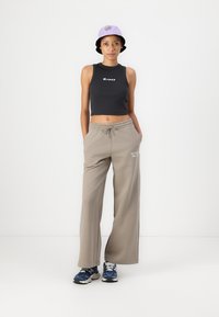 Black crop top with logo, beige wide-leg sweatpants, and a lavender bucket hat with logo; worn with blue sneakers.