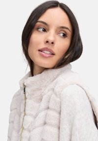 Helles rosa Kunstfelljacke mit quilteter Textur, hohem Kragen und silbernen Reißverschlussdetails. Weiches Material mit glatter Oberfläche.