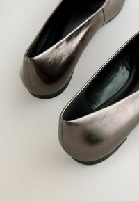 Bailarinas metálico gris con una textura de piel suave, punta redondeada, tacón bajo y un diseño sin costuras a lo largo de los bordes.