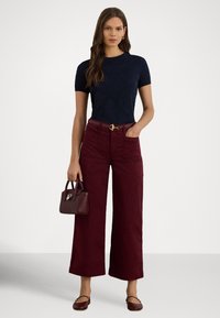 Tumši zils īsroku tops, plati bordo bikses ar kabatām un neliela bordo rokassoma. Apģērbu noslēdz brūnas dzīvokļveida kurpes.