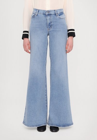 Jean flare taille haute bleu clair avec une texture en denim lisse et des jambes larges, présentant un design classique à cinq poches et une fermeture éclair à l'avant.