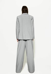 Szary, dopasowany żakiet i spodnie o szerokich nogawkach widziane od tyłu. Gładka tkanina z wyraźnie zarysowanymi ramionami oraz kontrastujący czarny top pod spodem.