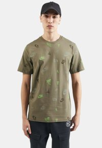 Camiseta de algodón verde oliva con logotipos de Nike dispersos en negro y verde neón. Mangas cortas, cuello redondo, ajuste relajado, diseño sencillo.