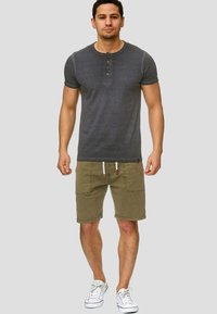 Dark grey short-sleeve henley shirt with wooden buttons, paired with olive green shorts featuring two front pockets and drawstring detail.