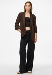 Hnedý blejzer s klopami over black crop top; spárovaný so širokými čiernymi džínsami a svetlohnedými sandálmi. Hladká, štruktúrovaná tkanina.