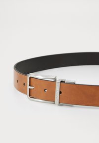 Ceinture en cuir brun avec intérieur noir, dotée d'une boucle en métal argenté et de multiples trous pour ajustement. Texture lisse et design simple.