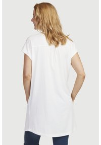 Hvid kortærmet tunika med rundet kant og sammensyning bagpå, lavet af blødt materiale. Båret med blå jeans.