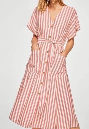 Femme portant une robe boutonnée jusqu'aux genoux avec des rayures verticales roses et blanches, manches courtes, ceinture et poches avant.