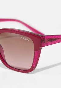 Różowe akrylowe okulary przeciwsłoneczne z gradientowymi soczewkami, teksturowane z dodatkiem brokatu, z logo "vogue" na oprawkach i zausznikach. Kąpielowy design.