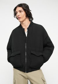 Schwarze gesteppte Bomberjacke mit Stehkragen, Frontreißverschluss und zwei Klappen-Taschen. Schlankes, gepolstertes Design mit gerippten Bündchen und Saum.
