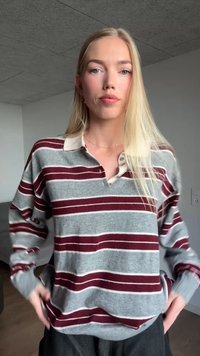 Siv pulover z maroon in belimi črtami, ovratnikom, dolgimi rokavi in sproščenim krojem. Ima detajl gumbov na ovratniku.