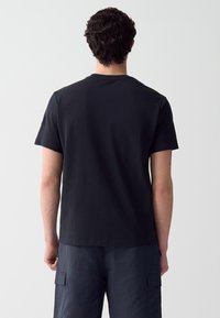T-shirt in cotone nero con maniche corte, scollo tondo e vestibilità relaxed. Tessuto morbido con dettagli minimi sul retro.